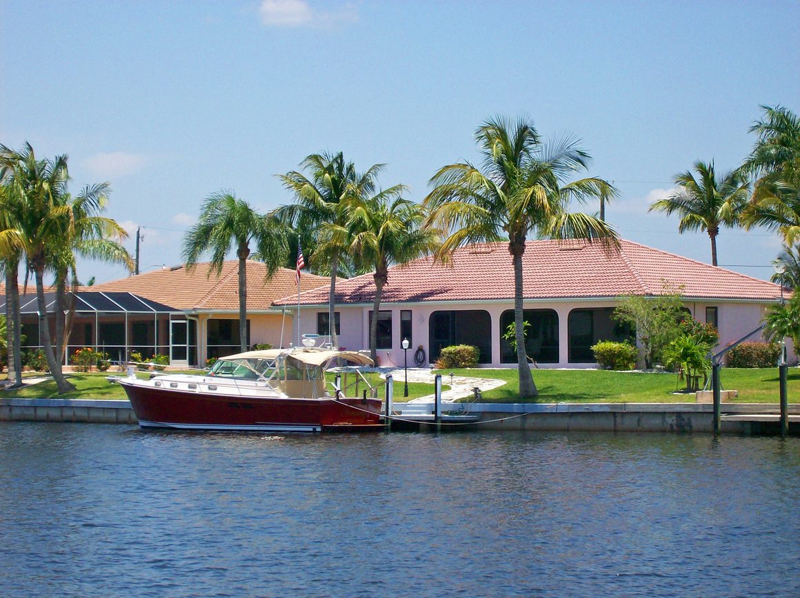 Blick über einen Frischwasserkanal auf eine Yacht mit Villen im Hintergrund