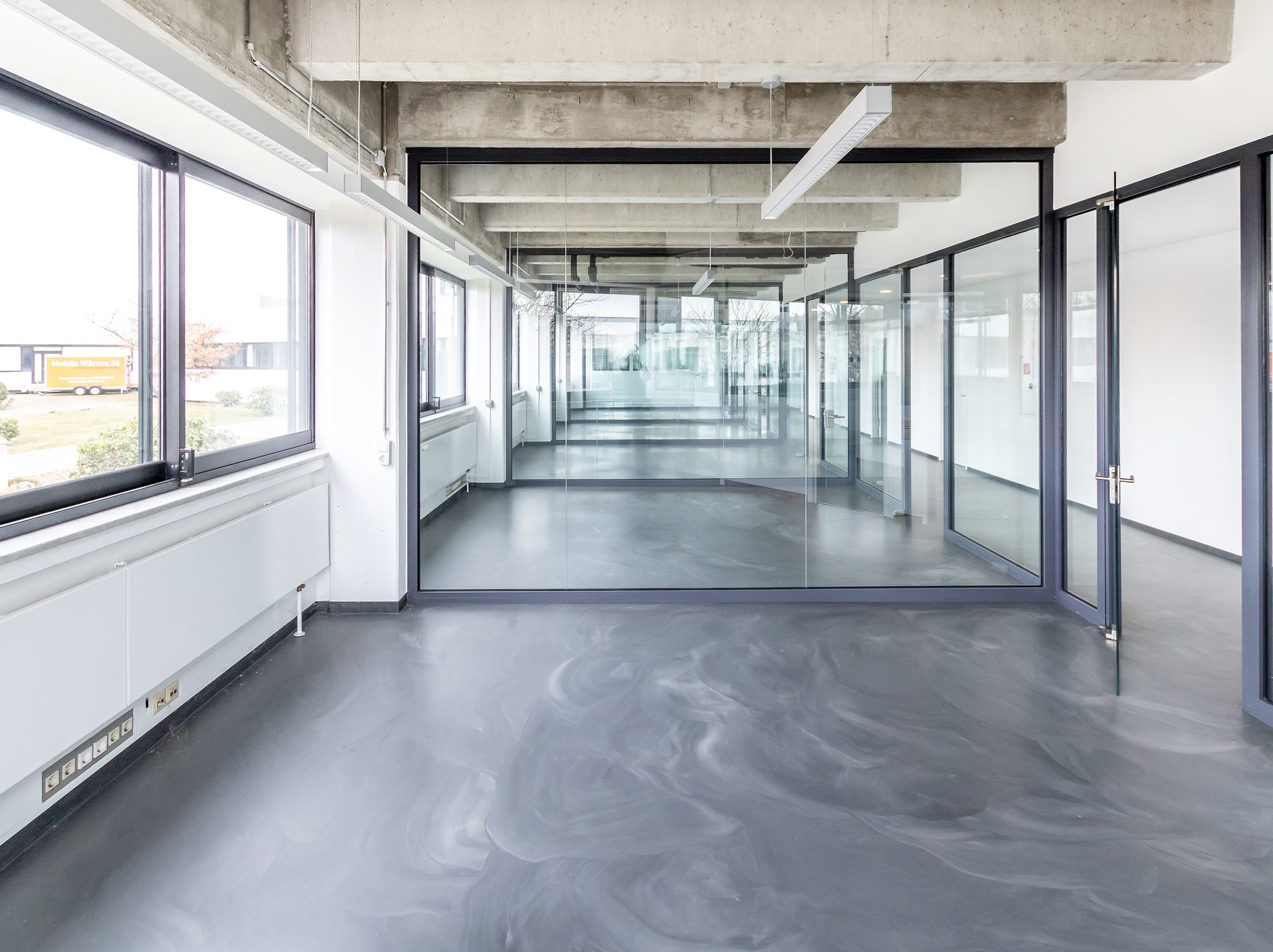 Drohnenaufnahme eines modernen Fachmarktzentrums mit großem Parkplatz und viel Grünflächen