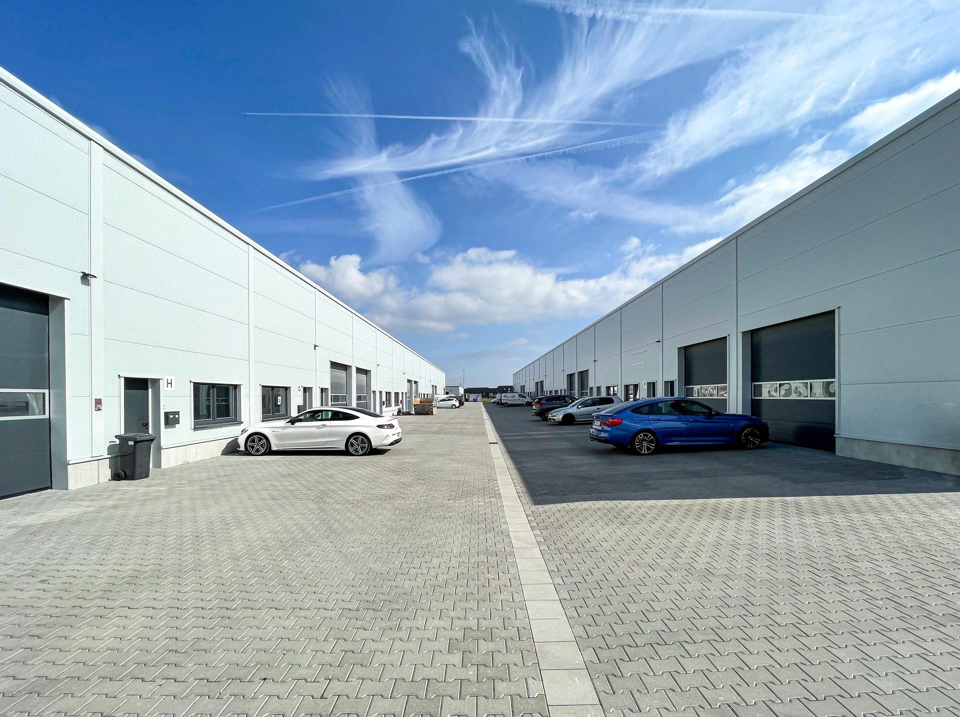 Drohnenaufnahme eines modernen Fachmarktzentrums mit großem Parkplatz und viel Grünflächen