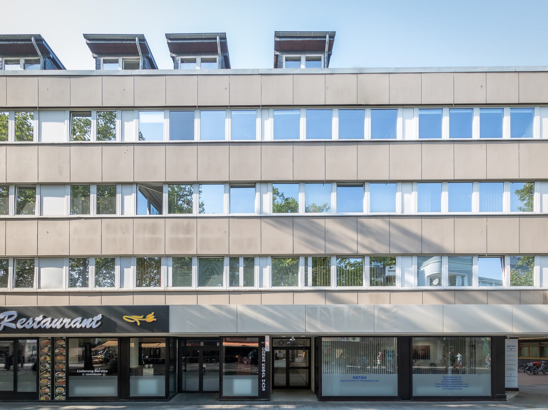 Drohnenaufnahme eines modernen Fachmarktzentrums mit großem Parkplatz und viel Grünflächen