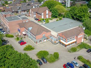 Drohnenaufnahme eines modernen Fachmarktzentrums mit großem Parkplatz und viel Grünflächen