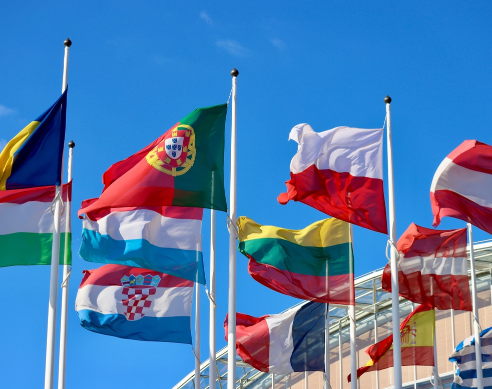 Gruppe von EU-Mitgliedsstaaten-Flaggen wehen im Wind vor dem EIB-Gebäude in Luxemburg: Rumänien, Ungarn, Portugal, Polen, Luxemburg, Frankreich, Litauen, Lettland, Österreich, Spanien, Kroatien und Griechenland.